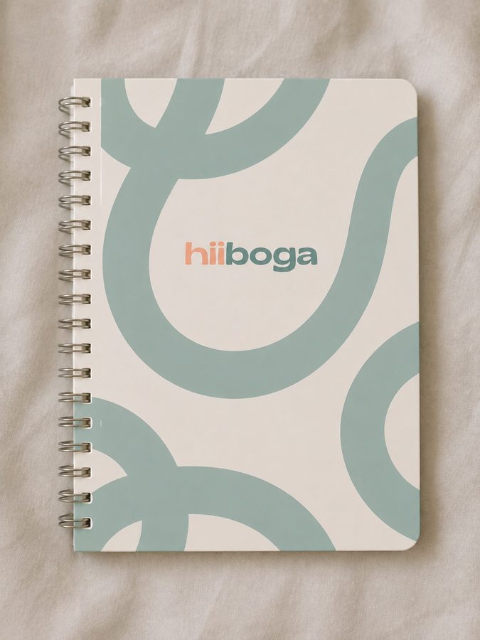 La agenda hiiboga: tapa color crema con curvas verde salvia y el logotipo en el centro, encuadernada con espiral.